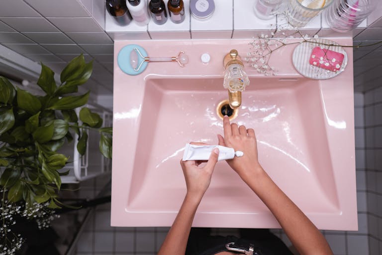 Top view of hands applying cream over a pink sink in a contemporary bathroom.